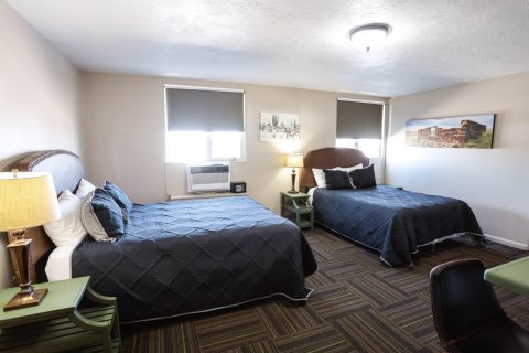 Spacious hotel room with two queen beds, window air conditioning, and local decor in Douglas WY.